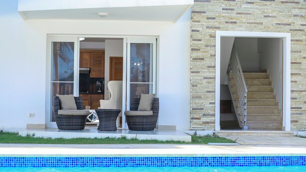 Una casa moderna con piscina, dos sillas de mimbre y una escalera que lleva a un nivel superior.