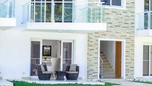 Una casa moderna de dos pisos con un balcón de vidrio, una piscina y mobiliario exterior.
