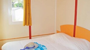 Yhden hengen sänky, jossa on valkoinen patja ja sininen peitto, olkihattu ja keltainen verho.