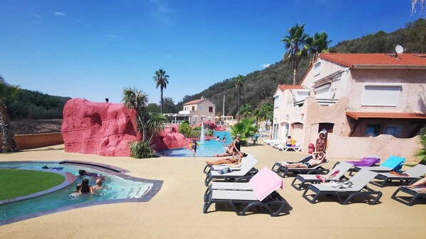 A resort pool area with lounge chairs, a rock formation, and a mountain backdrop.