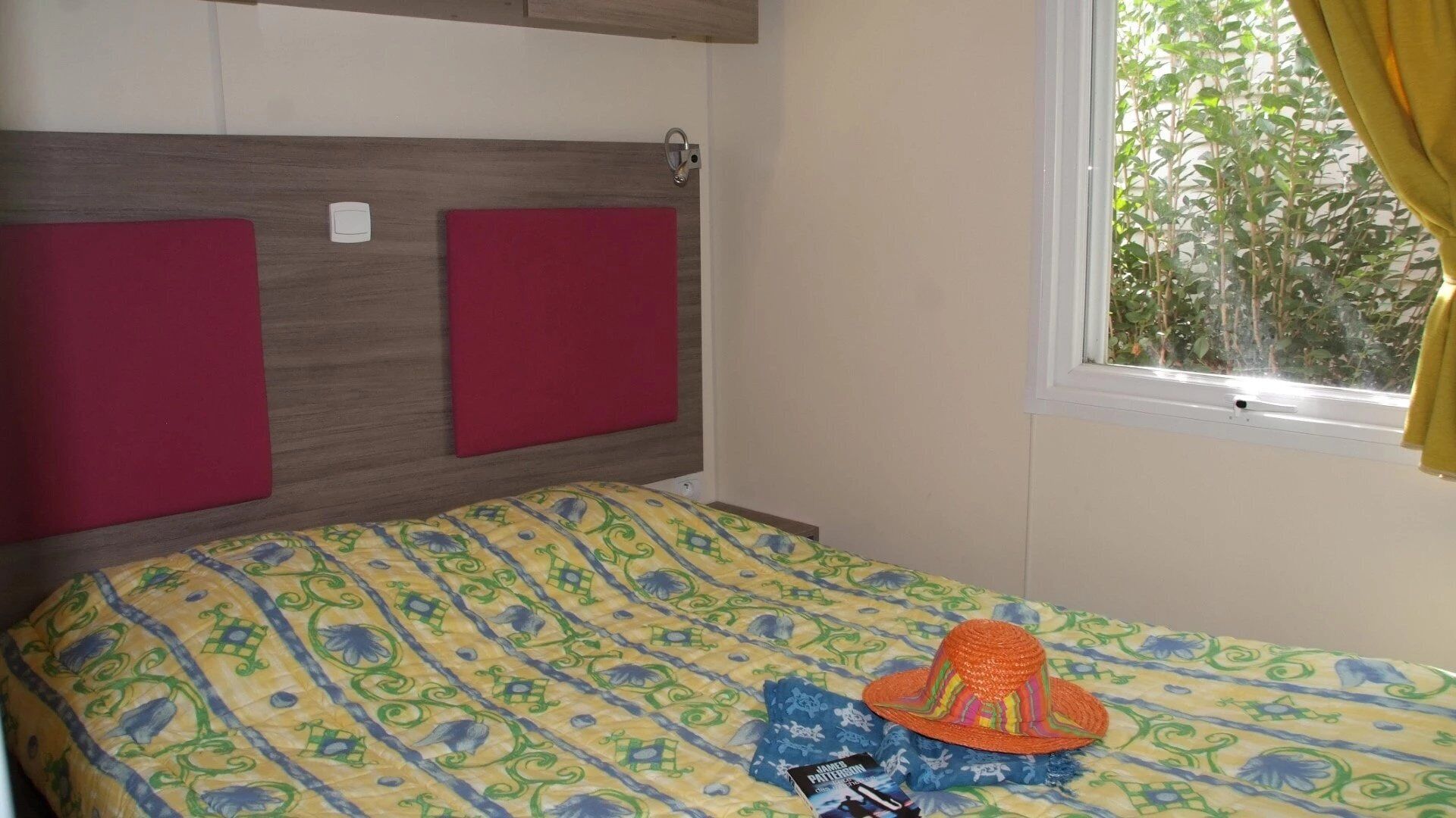 A bedroom with a bed, a window with curtains, and a view of greenery outside.