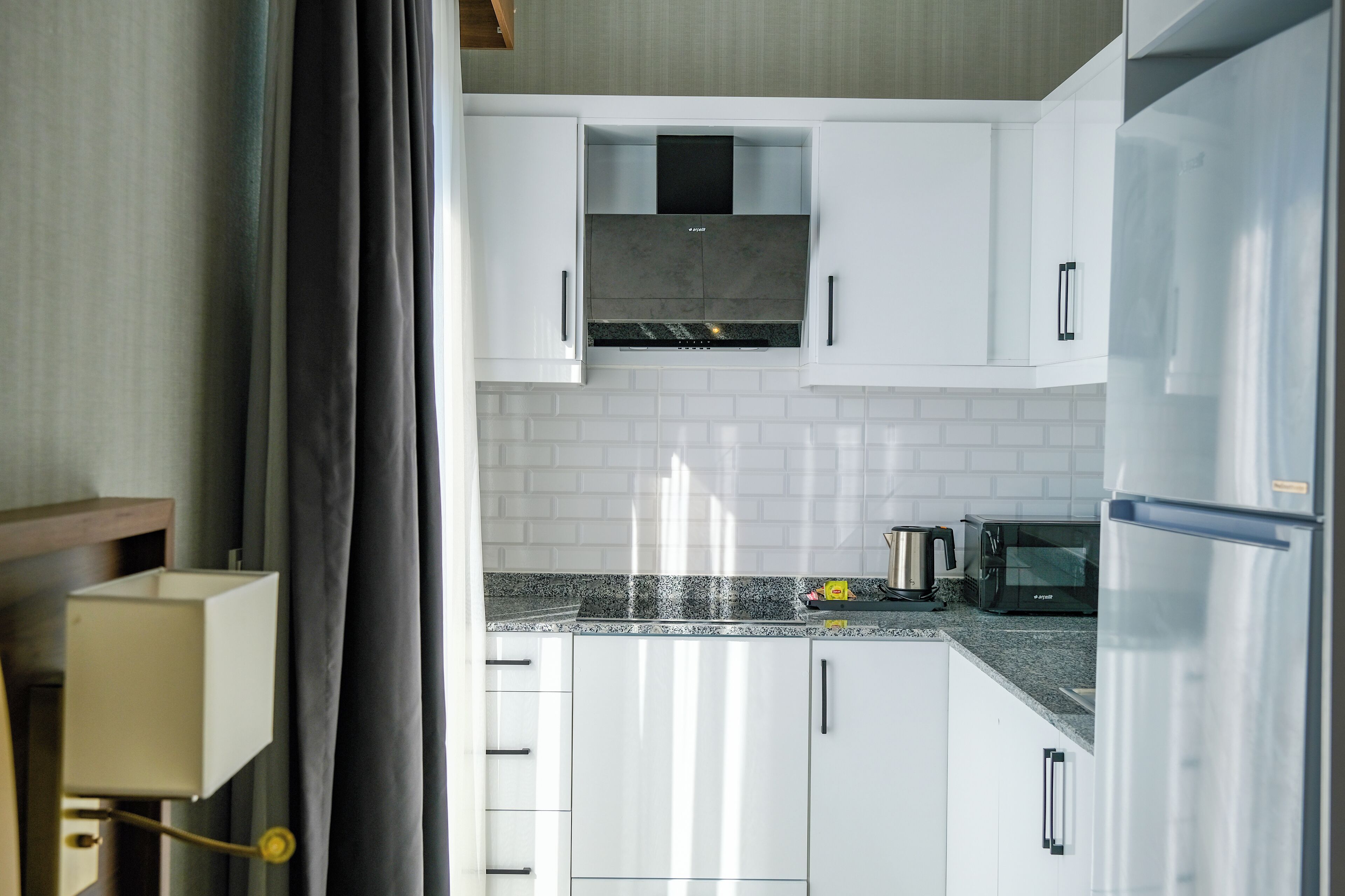 A modern kitchen with white cabinets, a stainless steel refrigerator, a microwave, and a built-in oven.