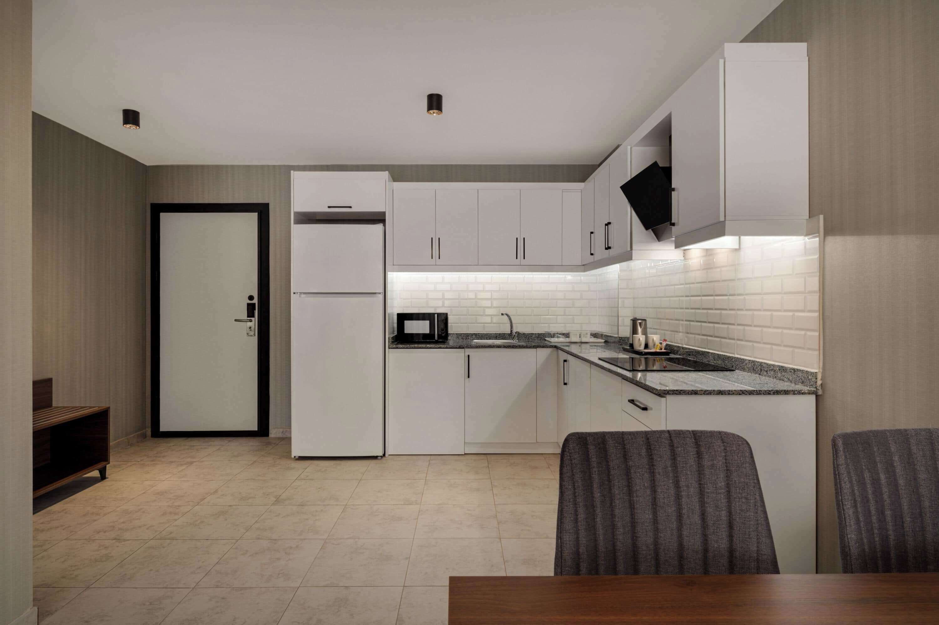 A modern kitchen with white cabinets, a black countertop, and a tiled backsplash. There is a dining area with a table and chairs.