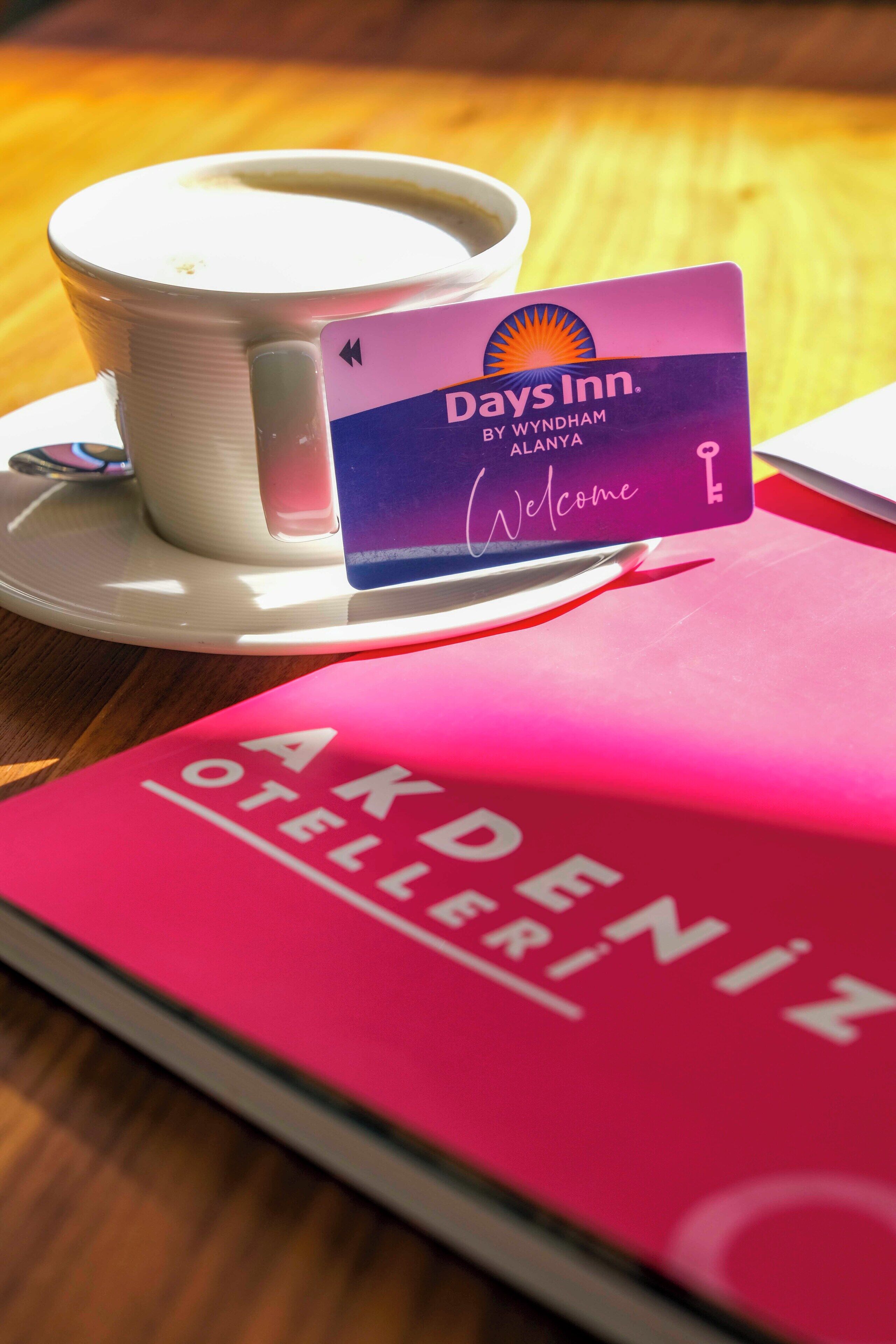 A Days Inn welcome card, a cup of coffee, and a pink book titled "AKDENIZ OTELLER".