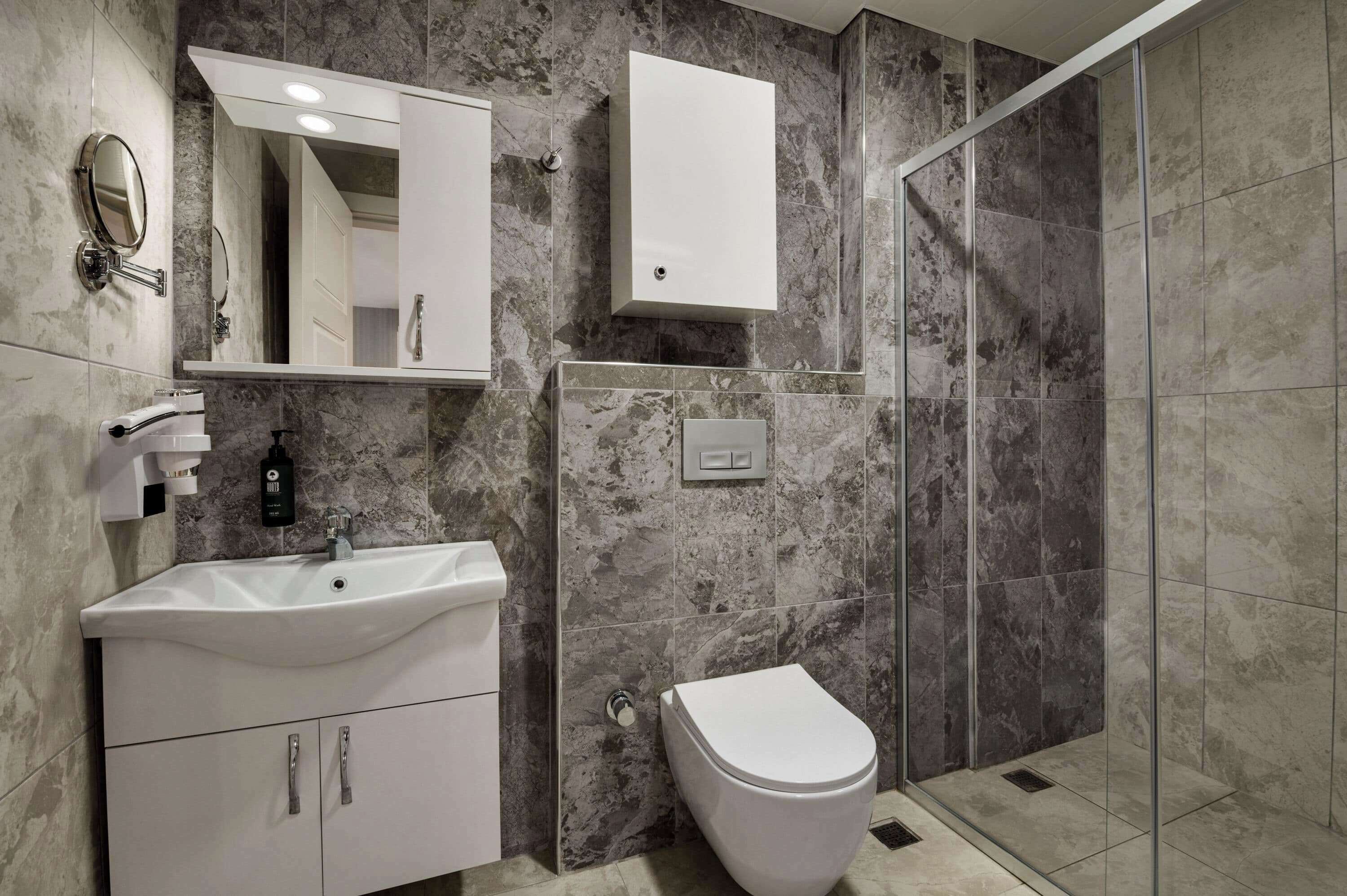 A modern bathroom with a white vanity, a mirror, a toilet, and a shower area with glass doors.