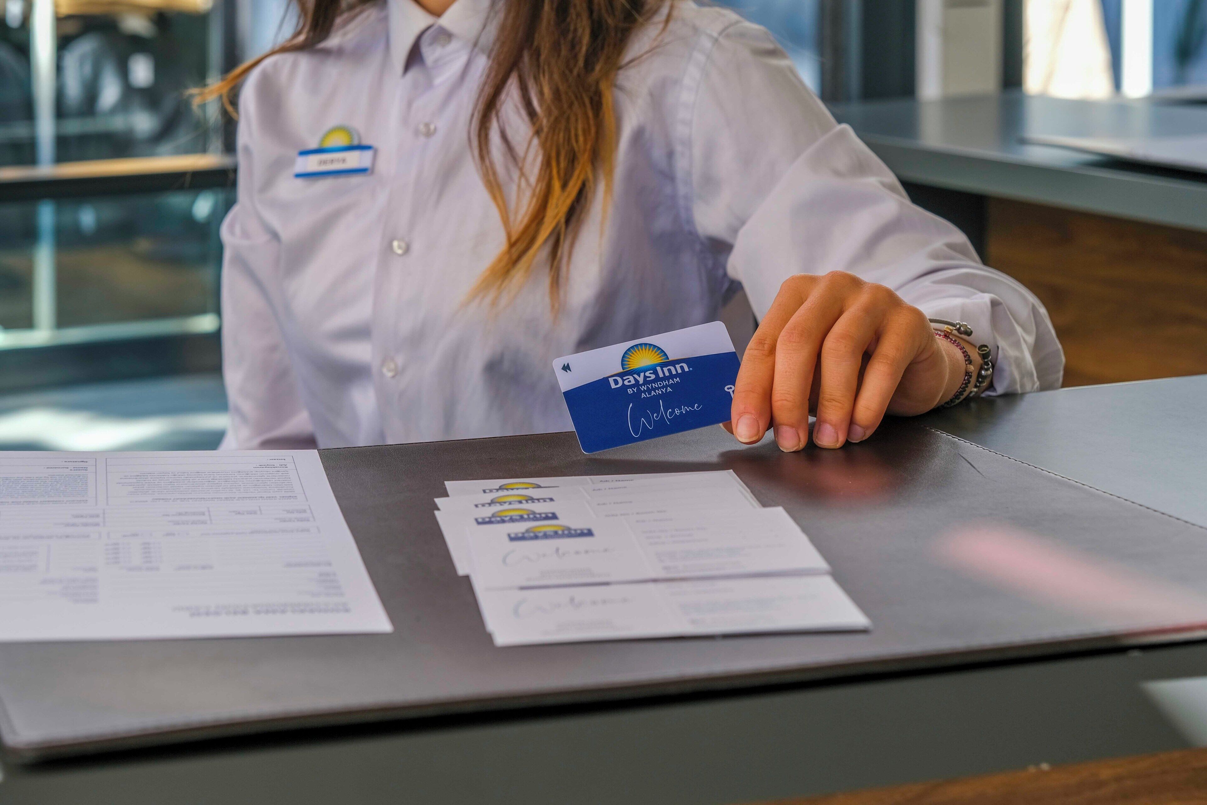 A person in a white shirt holding a card at a reception desk with paperwork.