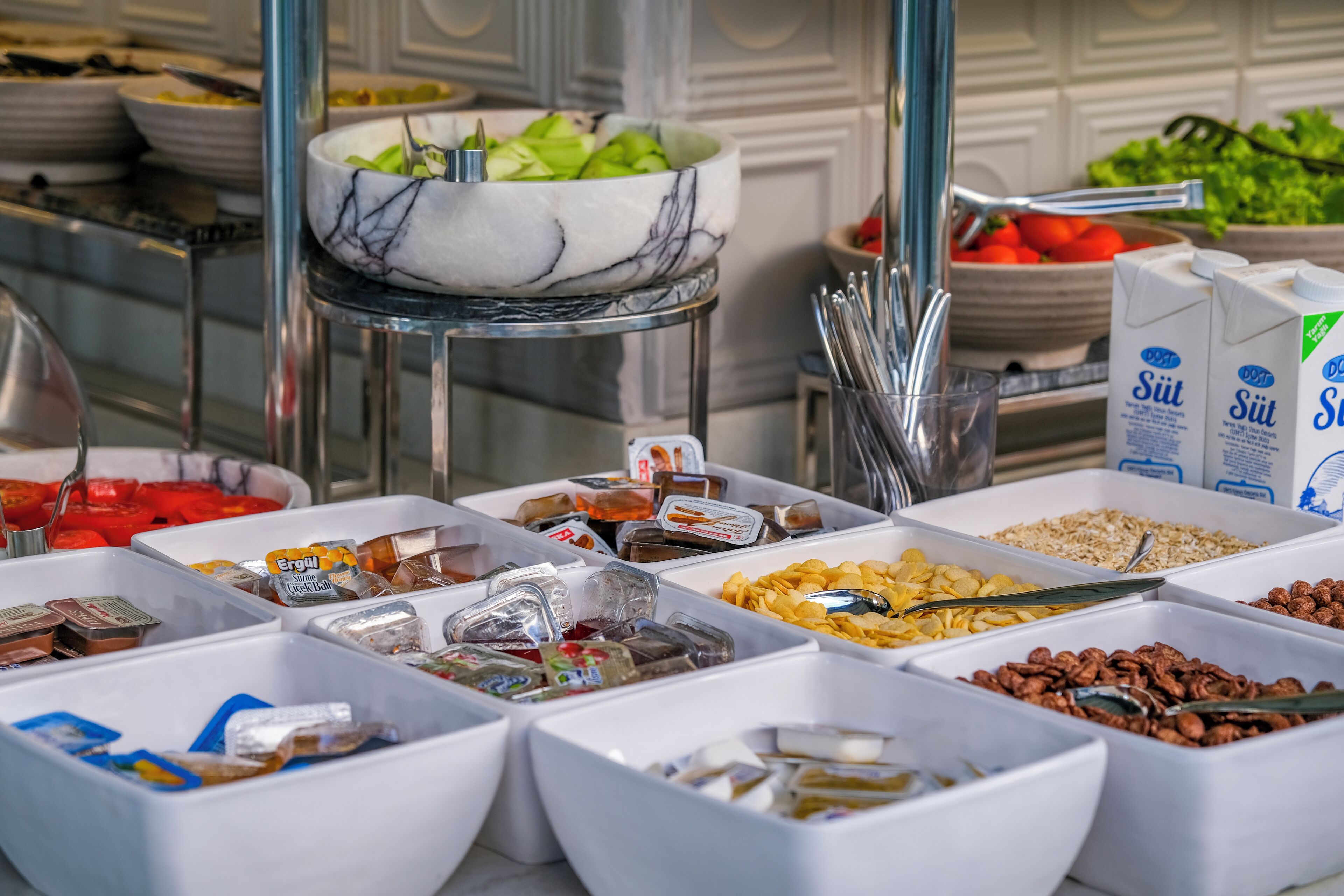 A buffet with various food items in white containers, including fruits, nuts, and cereals.