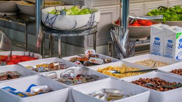 A buffet with various food items in white containers, including fruits, nuts, and cereals.