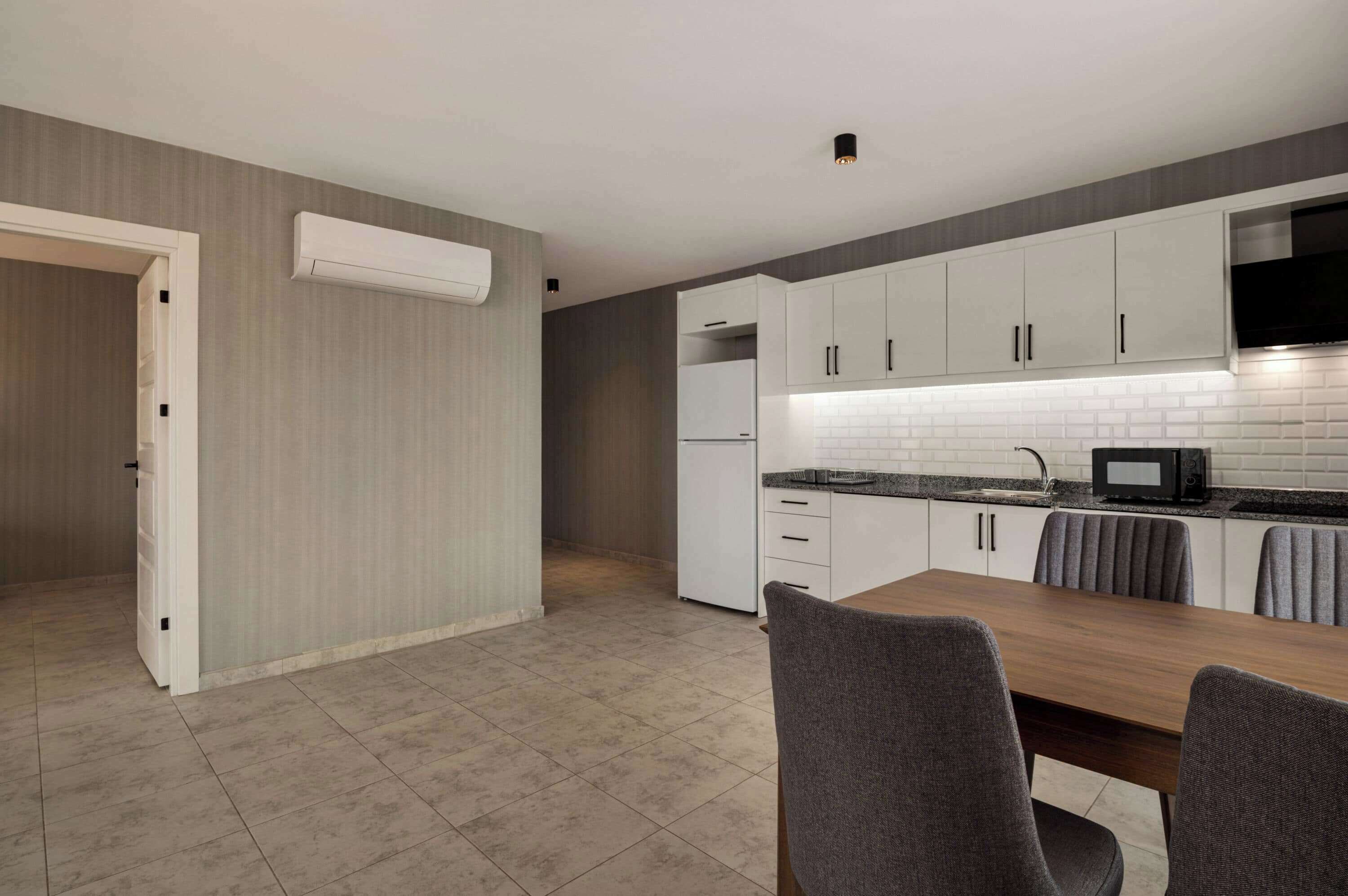 Una cocina moderna con armarios blancos, microondas integrado y un comedor con mesa de madera y sillas grises.