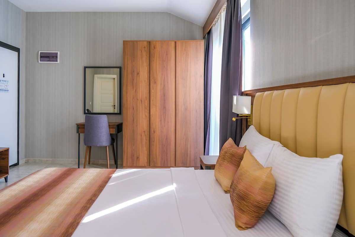 A hotel room with a large bed, a desk, a chair, a wardrobe, and a window with curtains.