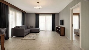 A modern living room with a sectional sofa, a flat-screen TV, and a large window with curtains. - Days Inn By Wyndham Alanya (Alanya)