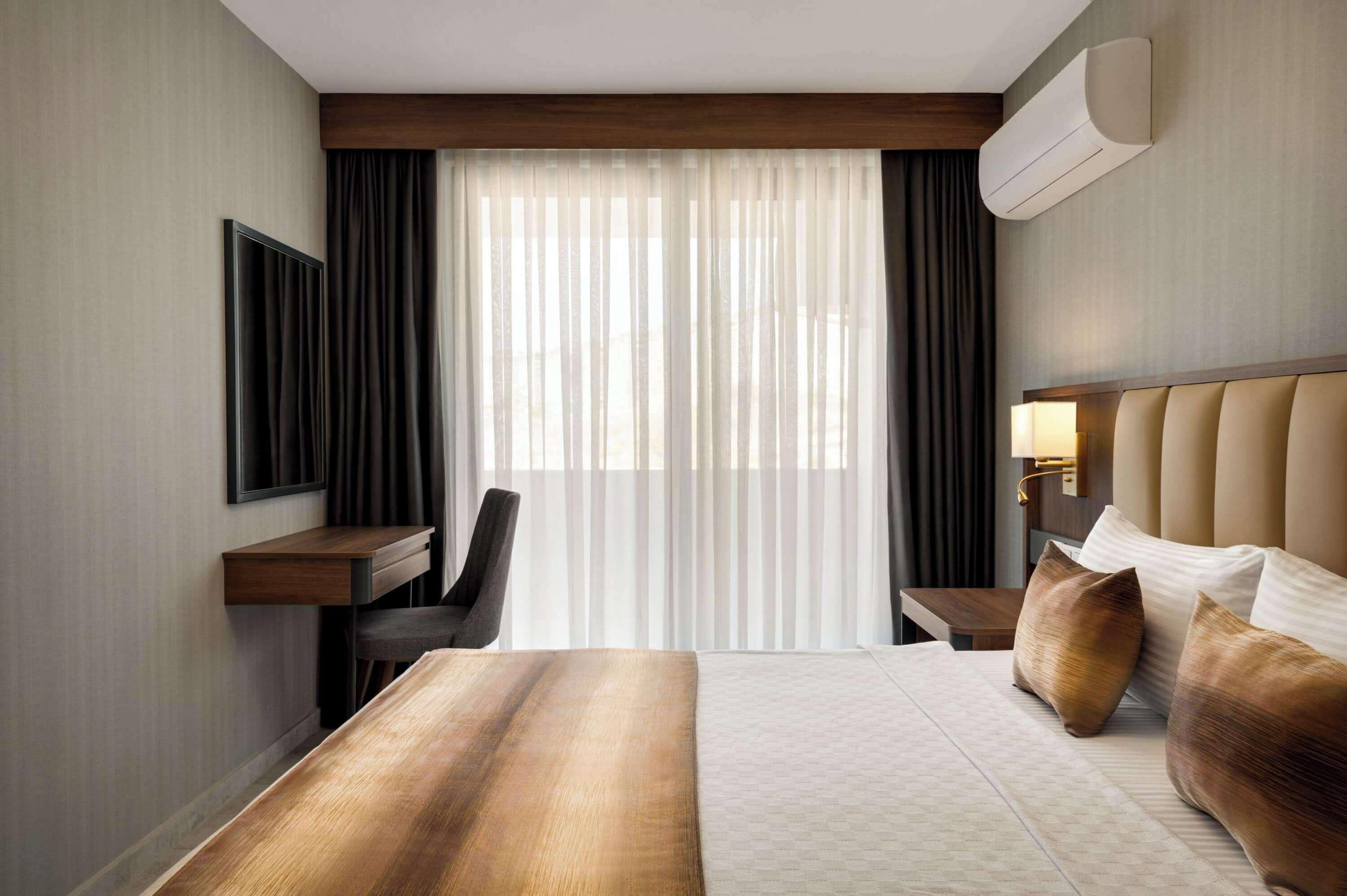 Habitación de hotel con cama, escritorio, silla, televisor y ventana con cortinas.