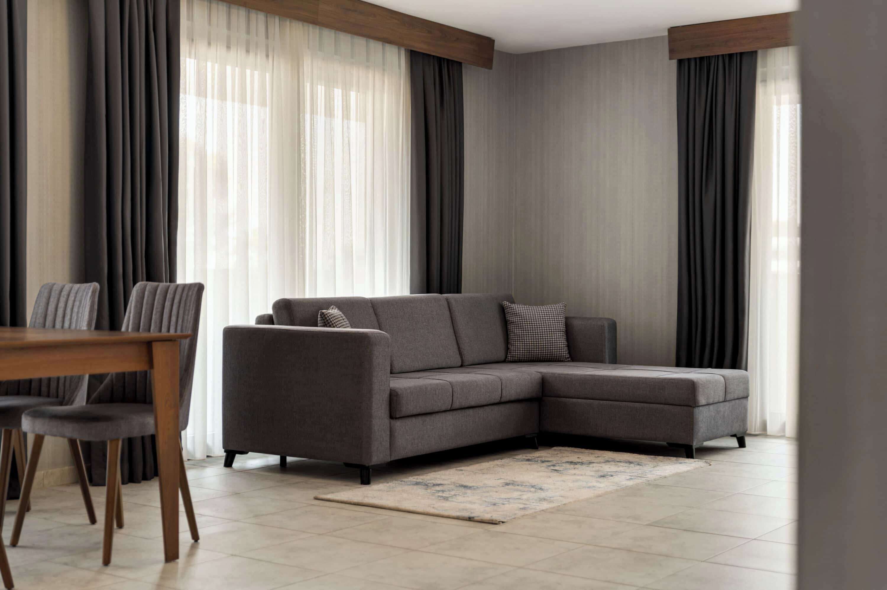 A modern living room with a grey sectional sofa, a wooden dining table with chairs, and a patterned rug.