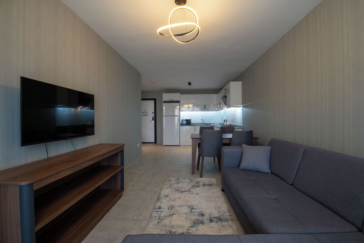 Una sala de estar moderna con un televisor de pantalla plana, un mueble de madera para entretenimiento, un sofá gris y una alfombra estampada.