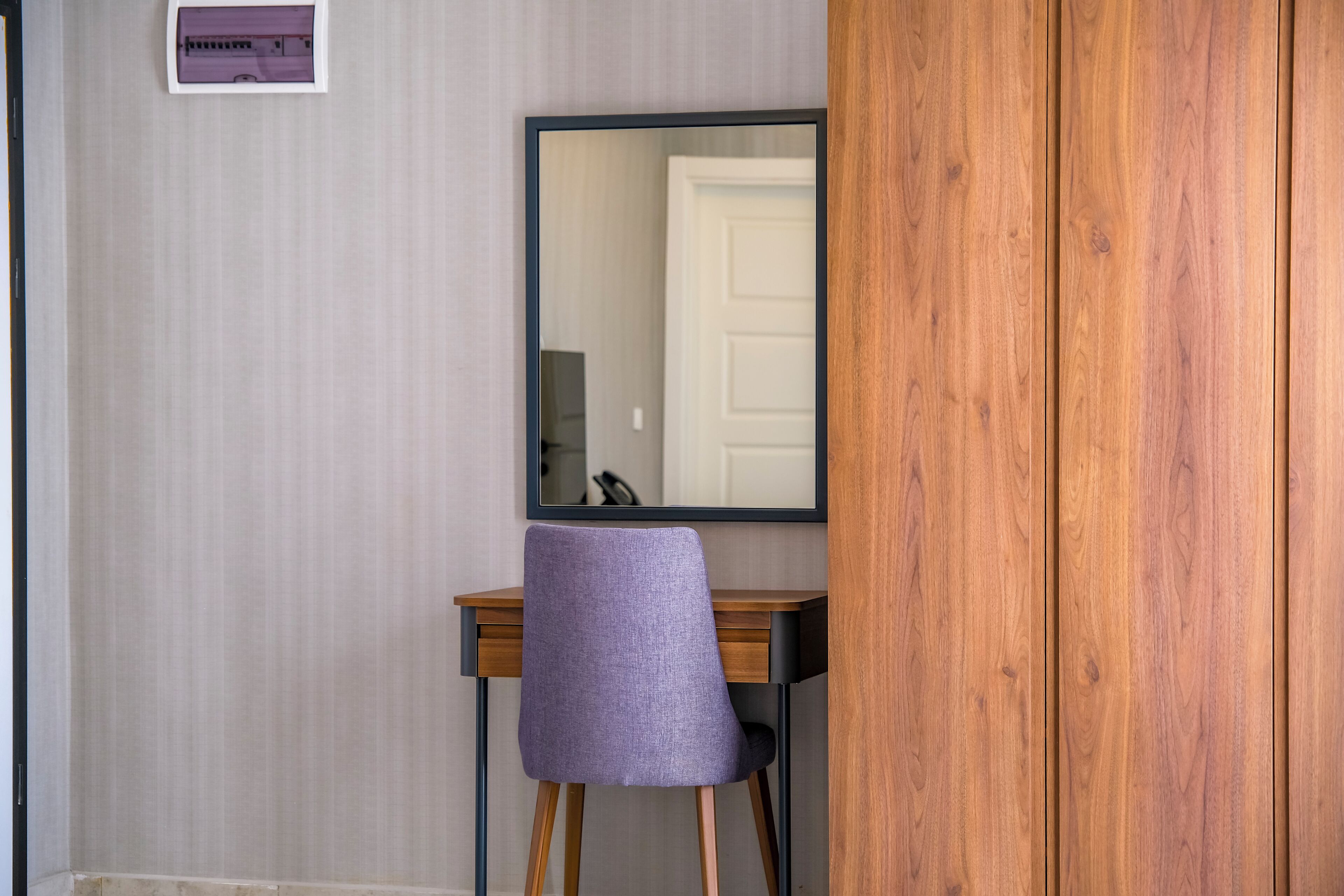 Una habitación con un escritorio de madera, una silla morada, un espejo y una puerta blanca.