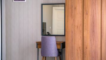 Una habitación con un escritorio de madera, una silla morada, un espejo y una puerta blanca.