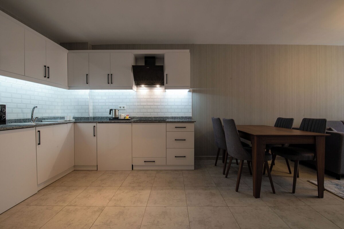 A modern kitchen with white cabinets, a black countertop, and a dining area with a wooden table and chairs.