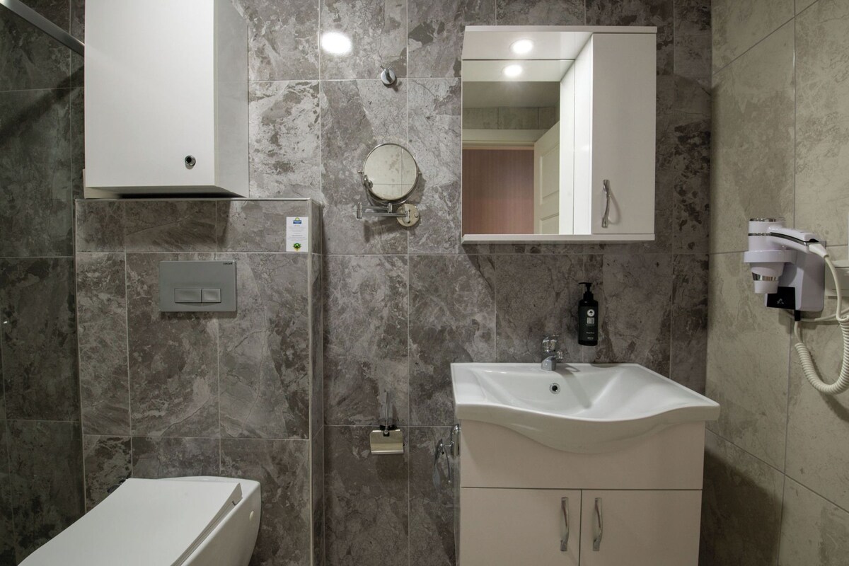 A modern bathroom with a white sink, a mirror, a shower, and a hairdryer.