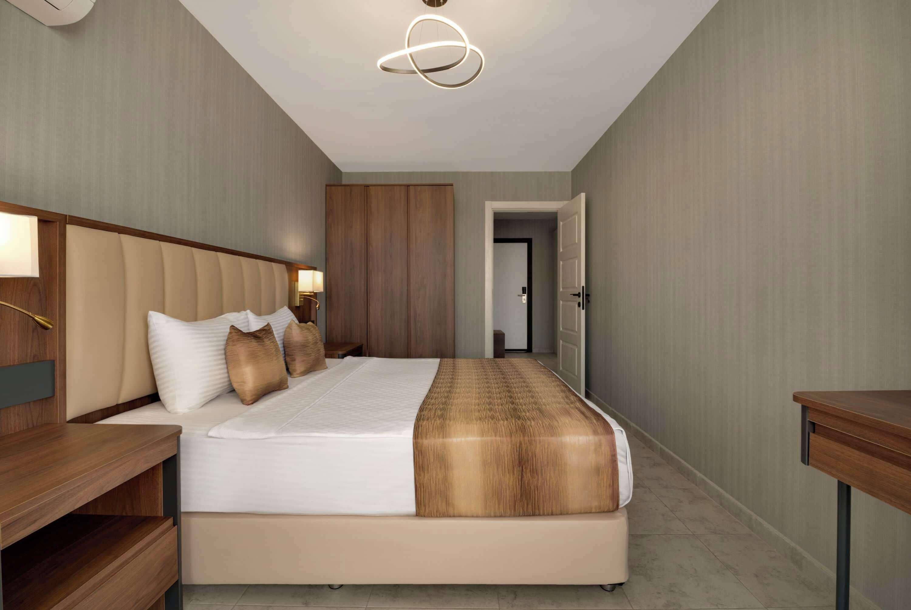 A hotel room with a large bed, a wooden headboard, a bedside table, and a modern light fixture.