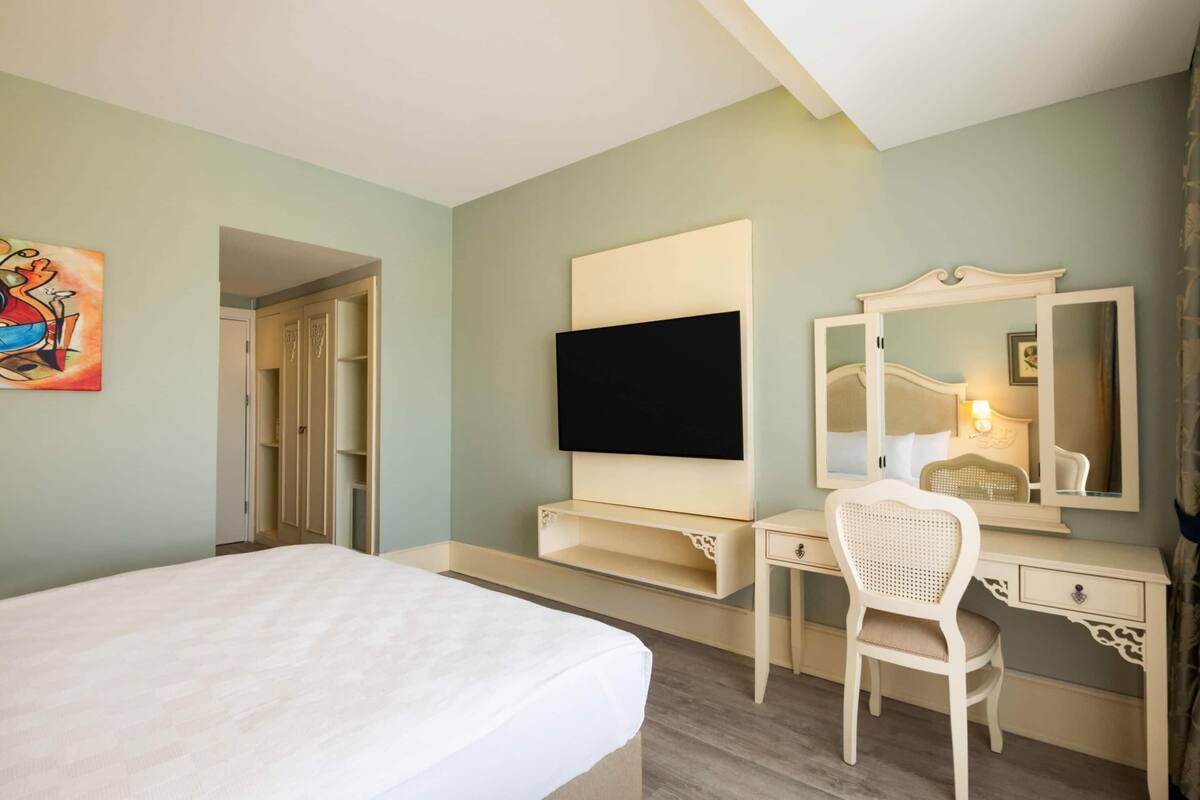 Ein Hotelzimmer mit einem Bett, einem Schreibtisch, einem Sessel, einem Fernseher, einem Spiegel und einem Kleiderschrank.