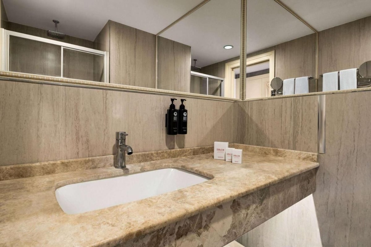 Un bany modern amb un lavabo de marbre, un mirall gran i productes de tocador.