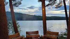 Un terrain de camping équipé d’un foyer, de deux bancs en bois et de guirlandes lumineuses.