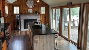 Une cuisine aux murs en bois, dotée d’un îlot central, d’une cuisinière intégrée et d’une grande fenêtre donnant sur une terrasse.