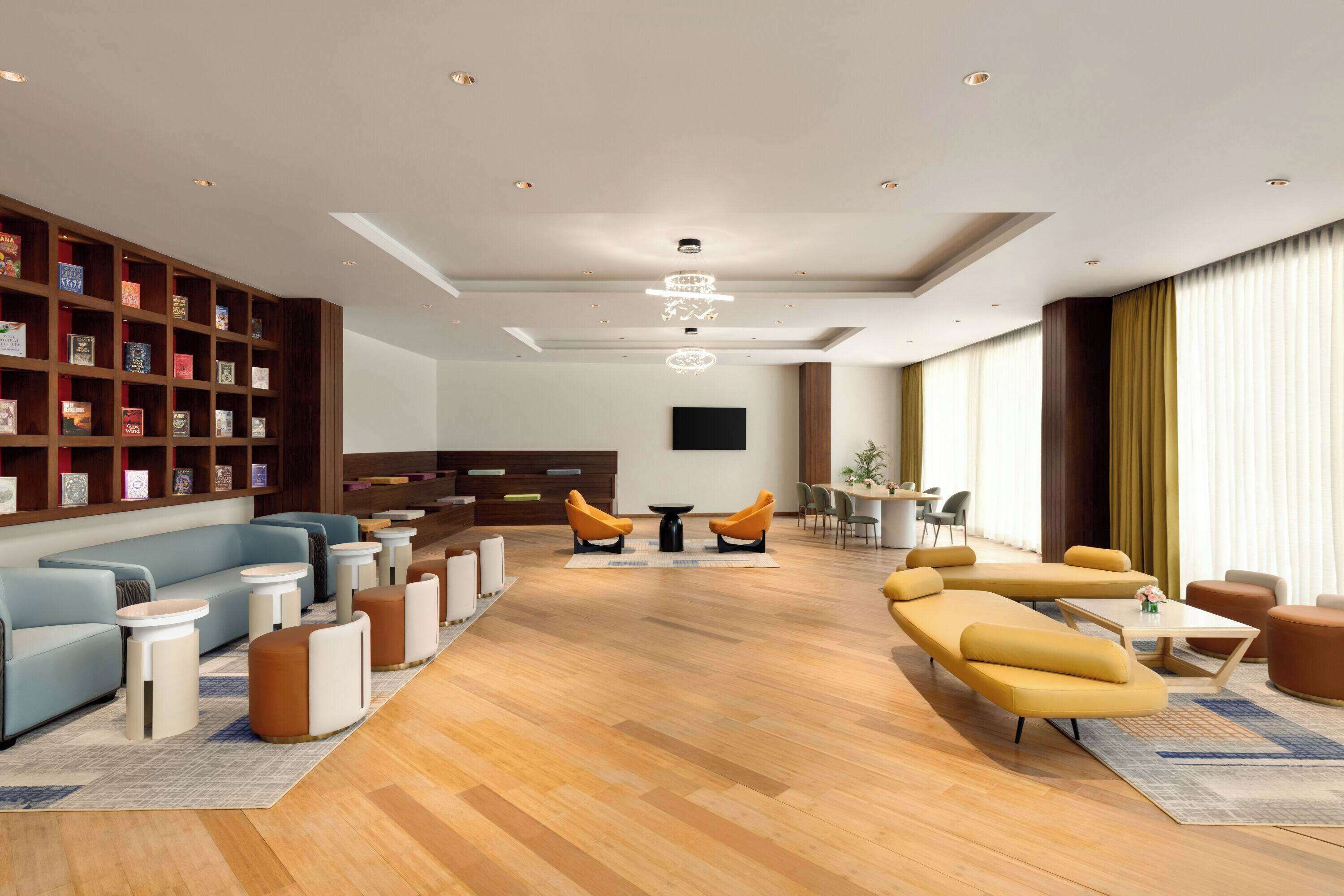 A modern hotel lobby with a central seating area, a bookshelf, and a flat-screen TV.