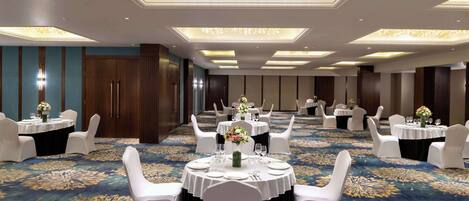 A banquet hall with round tables, white chairs, and chandeliers.