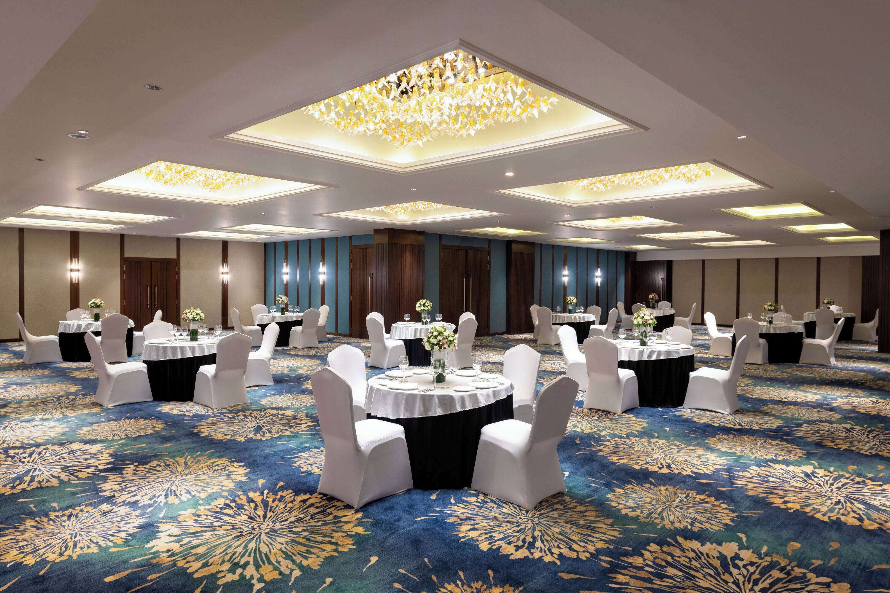 A large banquet hall with round tables and white chairs, featuring a blue carpet with a floral pattern.