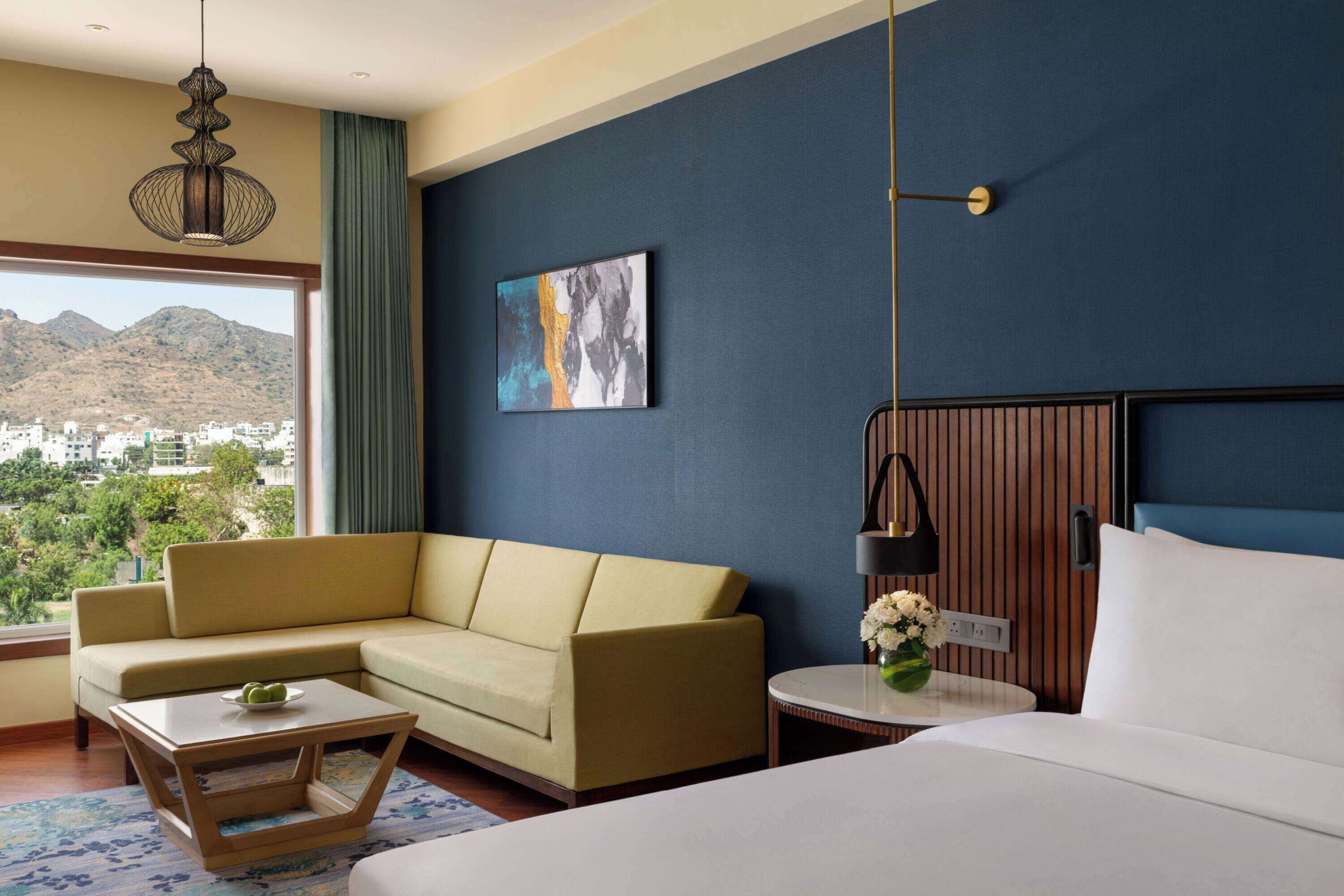 A hotel room with a bed, sofa, coffee table, and a painting on the wall.
