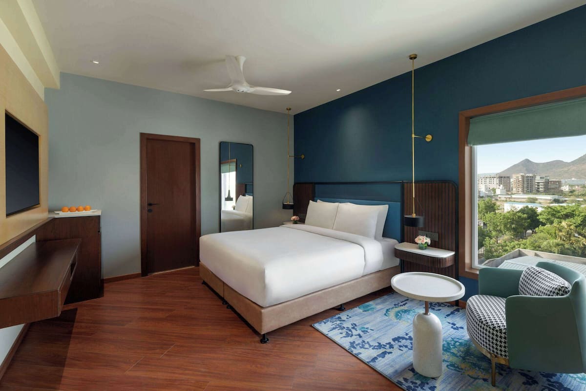 Een moderne hotelkamer met een groot bed, een bureau, een stoel en uitzicht op de stad.