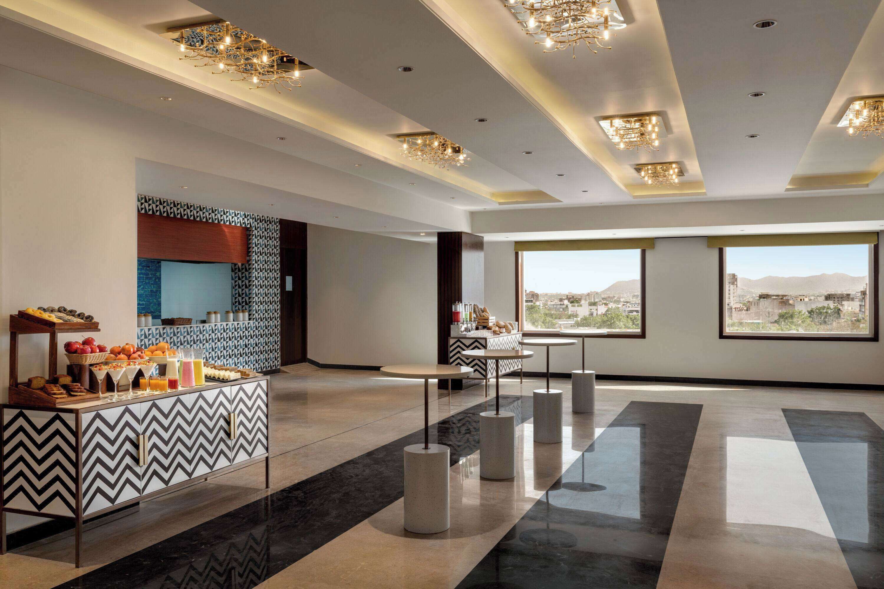 A modern hotel lobby with a buffet, large windows, and a city view.