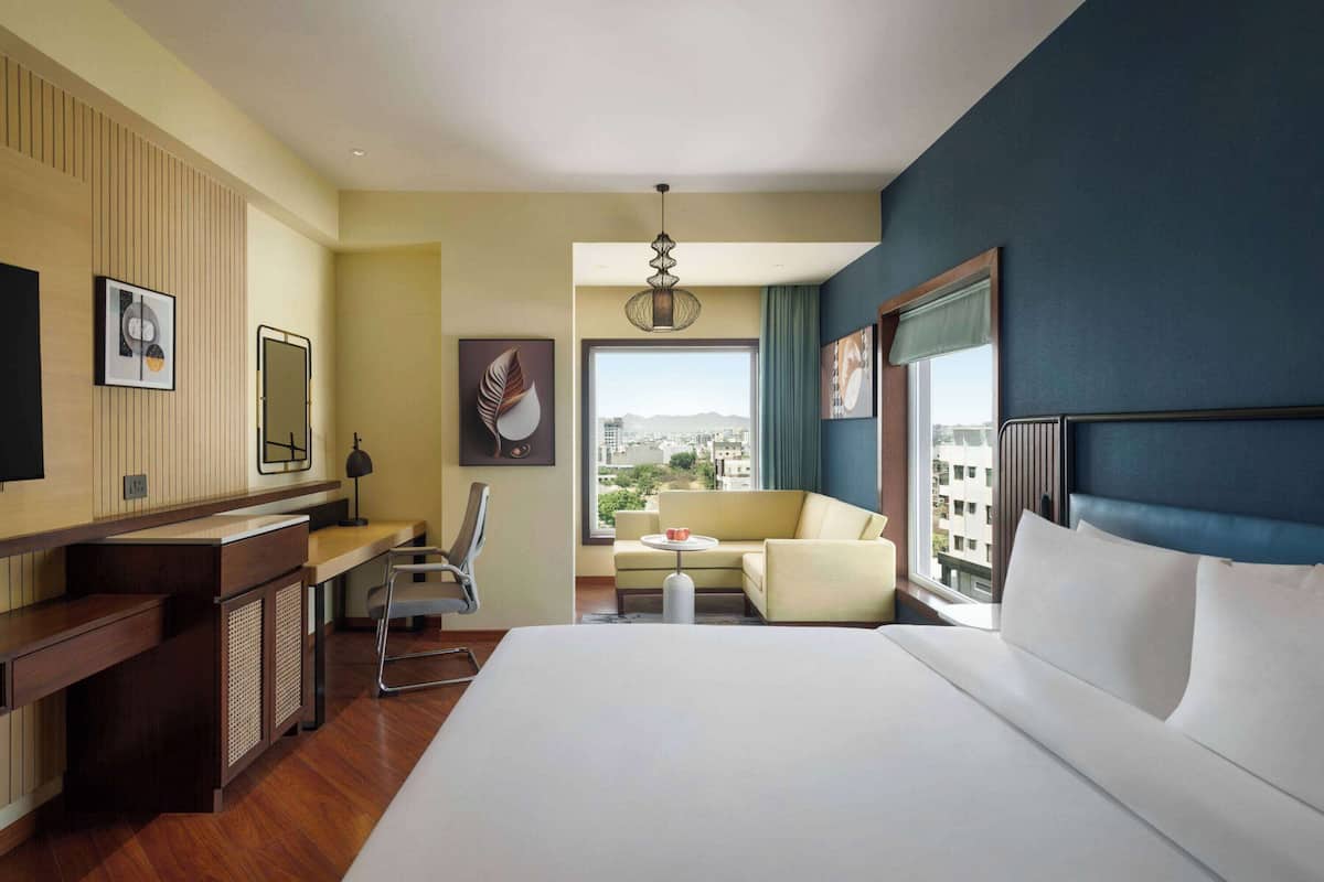 Een hotelkamer met een groot bed, een bureau, een stoel, een bank en uitzicht op de stad door het raam.