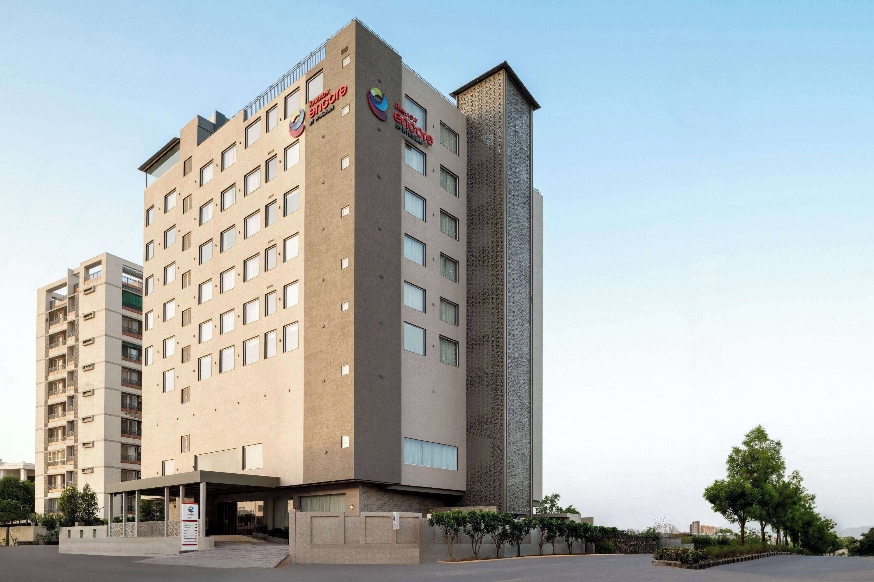 Un moderno edificio di un hotel con diversi piani, un ingresso ben visibile con tettoia e il logo di "Encore Hotels".