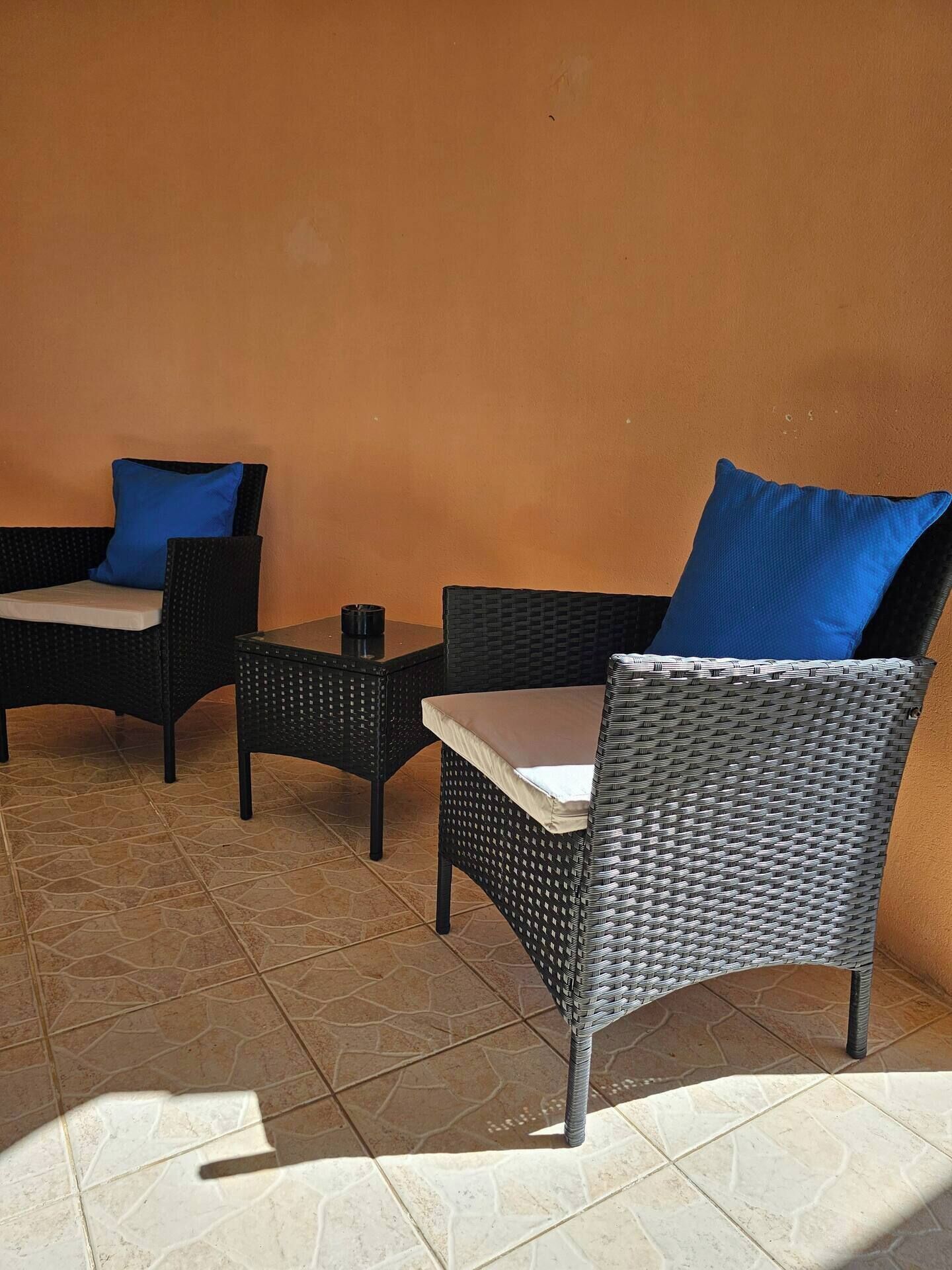 Een terras met rieten meubels en kussens, een betegelde vloer en een effen muur.