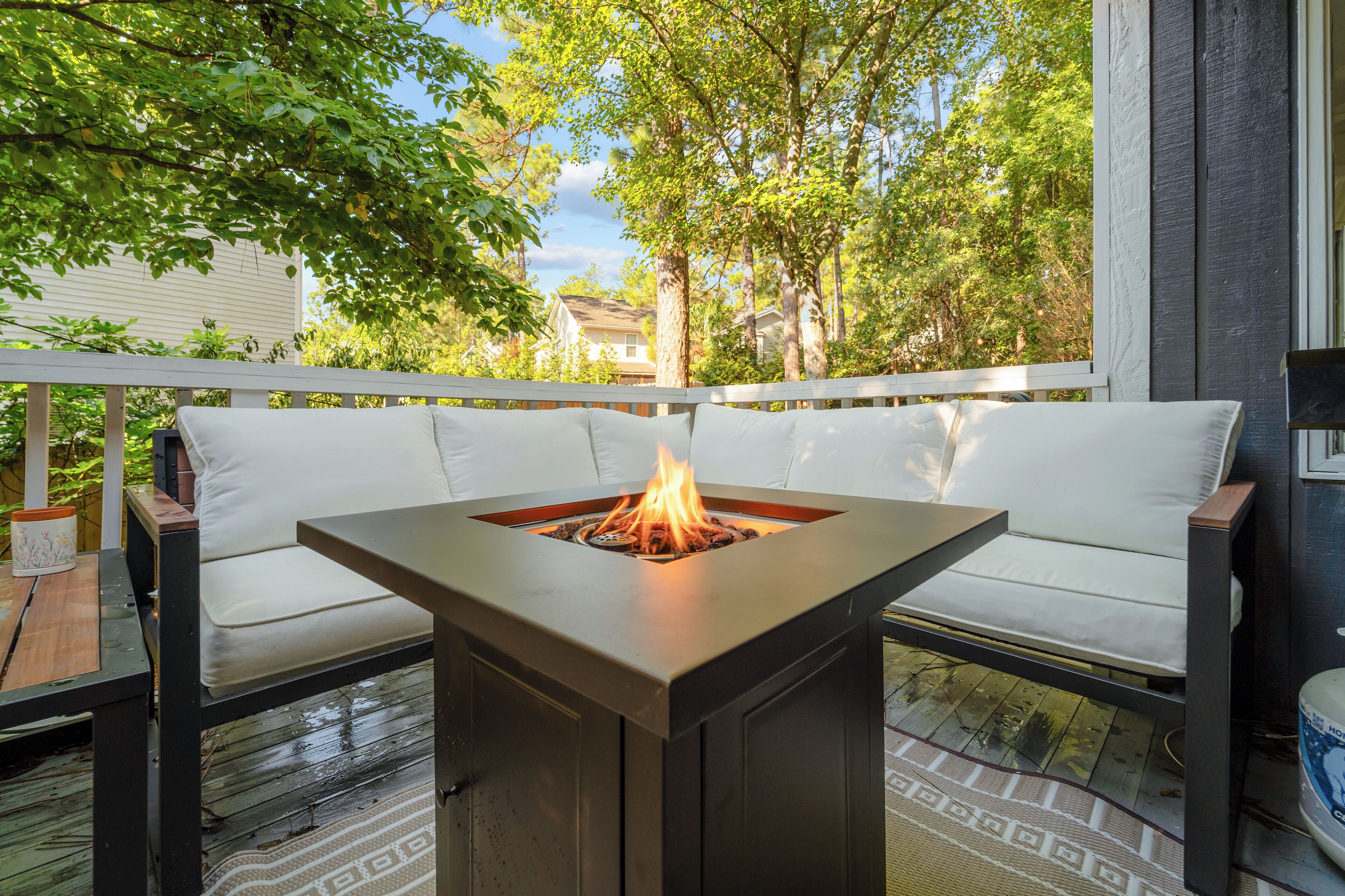 A deck with a square fire pit table surrounded by white cushioned seating.