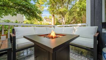 A deck with a square fire pit table surrounded by white cushioned seating.