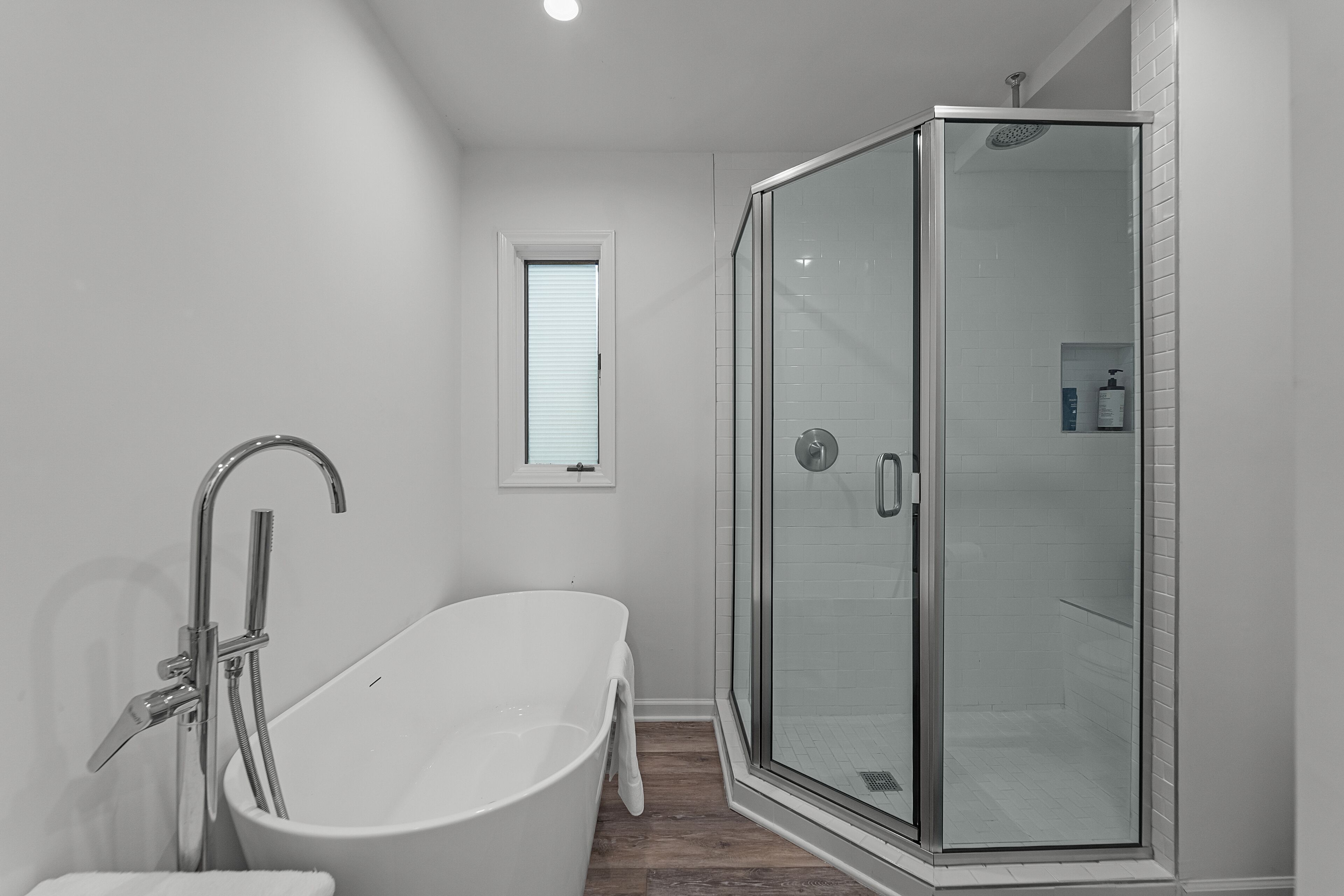 A modern bathroom with a freestanding bathtub, a glass-enclosed shower, and a small window.