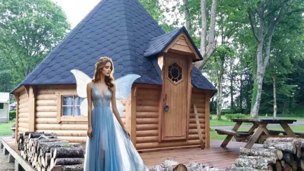 A log cabin with a steeply pitched roof, a wooden door, and a small window.