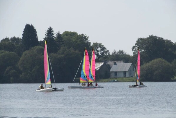 Three sailboats on a calm lake with a house in the background.