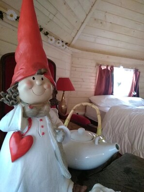 Ein gemütliches Zimmer mit einem Bett, einem Korbstuhl, einer dekorativen Gartenzwerg-Figur und einem Teekessel.