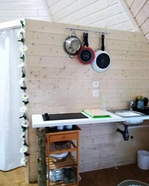 A kitchen with wooden walls, a white countertop, and a wooden shelf below. There are pots and pans hanging on the wall.