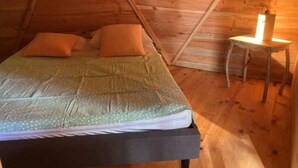 A cozy attic bedroom with a bed, pillows, and a small table with a lamp. - ZEcamping 3 étoiles animaux acceptés locatif 38m2 4 pers (Priziac)