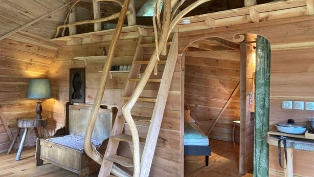 A wooden cabin interior with a spiral staircase, a bed, a small table, and a lamp. - ZEcamping 3 étoiles animaux acceptés locatif 38m2 4 pers (Priziac)