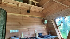 A wooden cabin interior with a kitchen area, including a stove, sink, and window with a view of greenery. - ZEcamping 3 étoiles animaux acceptés locatif 38m2 4 pers (Priziac)