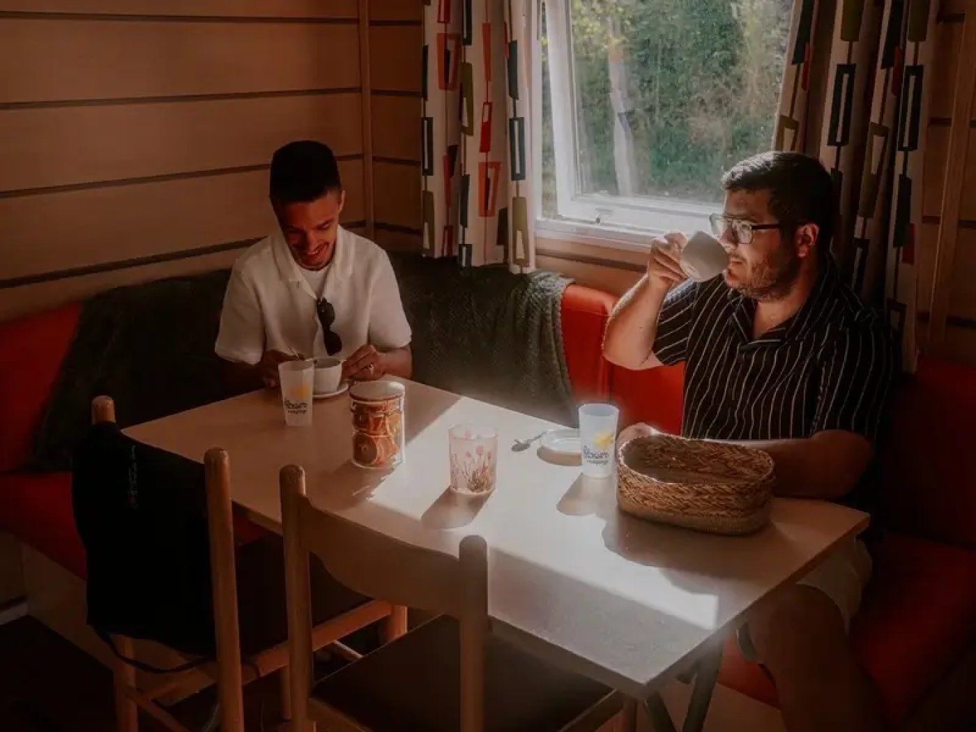 Two individuals seated at a table with a window view, a basket, and a candle.