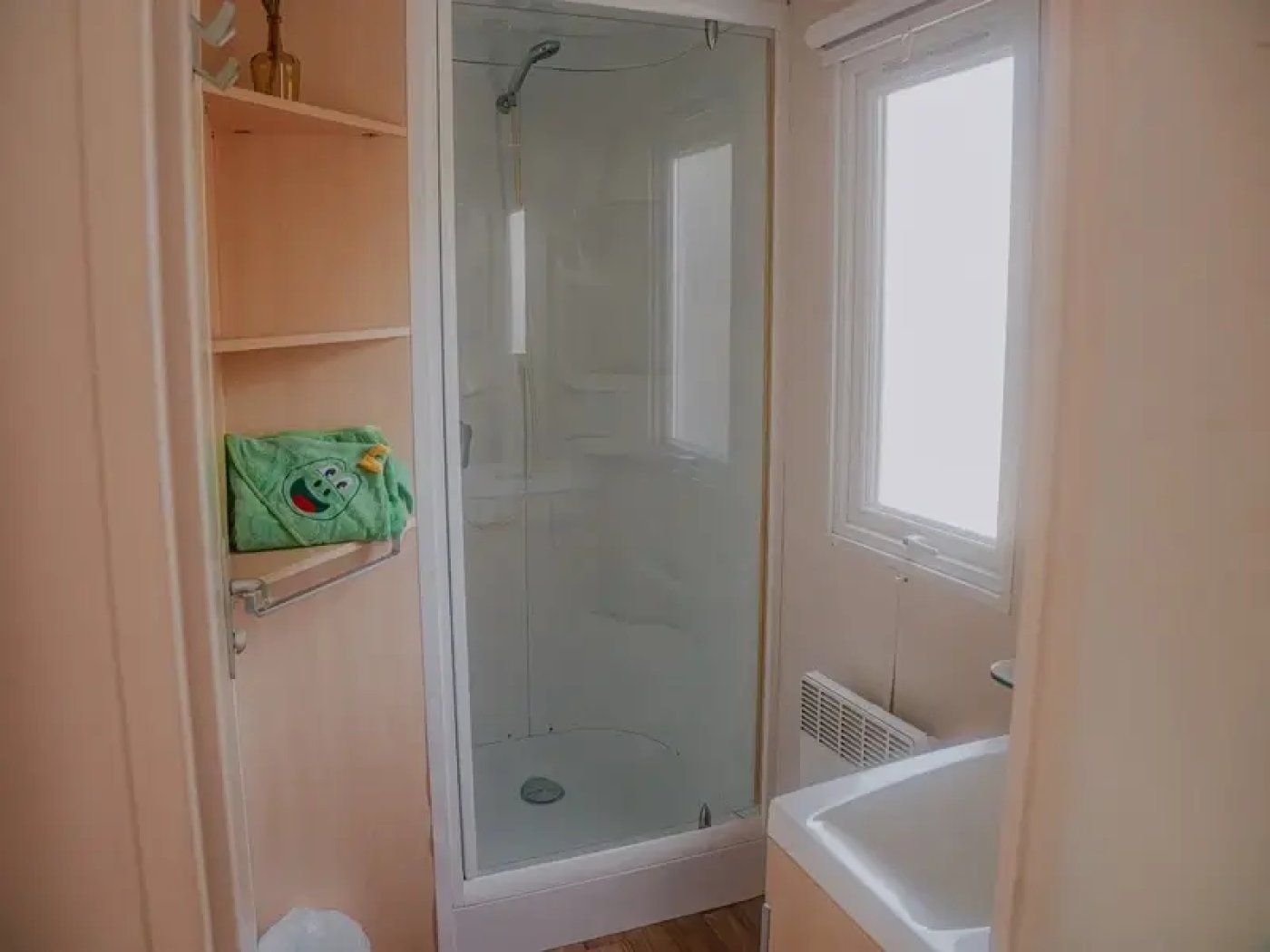 A bathroom with a glass-enclosed shower, a white bathtub, and a shelf with a green bag.