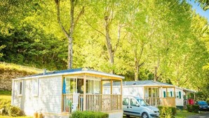 Une rangée de maisons mobiles dotées de terrasses en bois et de grandes fenêtres, entourées d’arbres verdoyants et luxuriants.