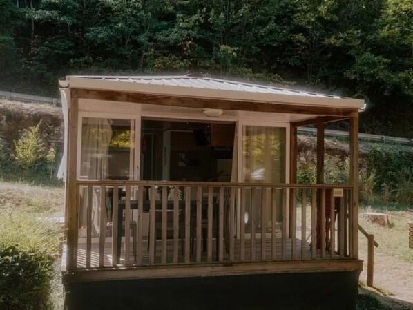 A small wooden structure with a balcony, surrounded by greenery.